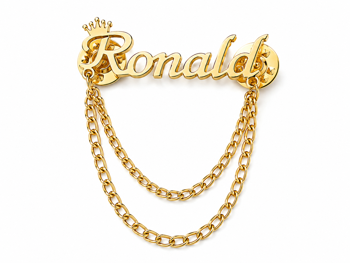 Pin’s AUDACE doré personnalisé avec le prénom Ronald, couronne et chaînes décoratives sur fond blanc