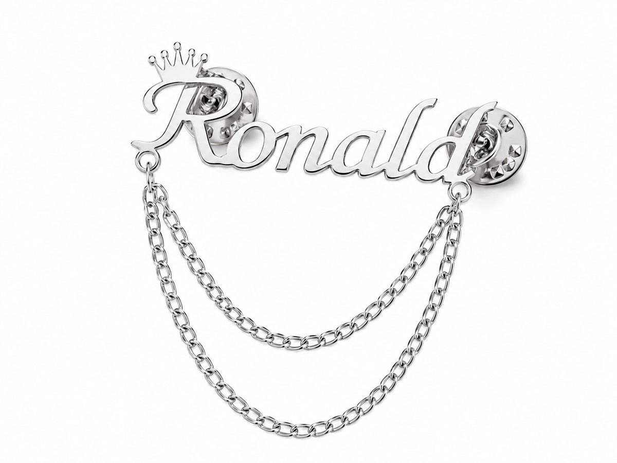 Pin’s AUDACE argenté personnalisé avec le prénom Ronald, couronne et chaînes décoratives sur fond blanc