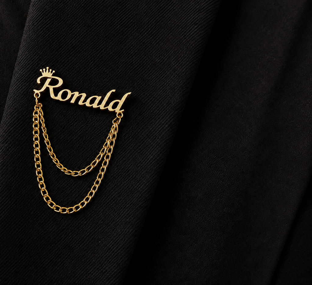 Pin’s AUDACE doré personnalisé avec le prénom Ronald, couronne et chaînes décoratives sur veste noire