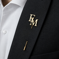 Pin’s à tige ÉLITE doré personnalisé avec les initiales EM porté sur une veste noire