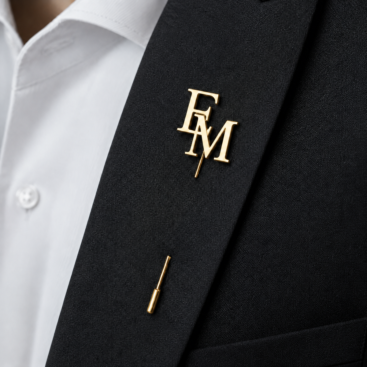Pin’s à tige ÉLITE doré personnalisé avec les initiales EM porté sur une veste noire