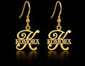 Boucles d’oreilles KOMORA dorées personnalisées avec grande initiale K et prénom Komora fond noir