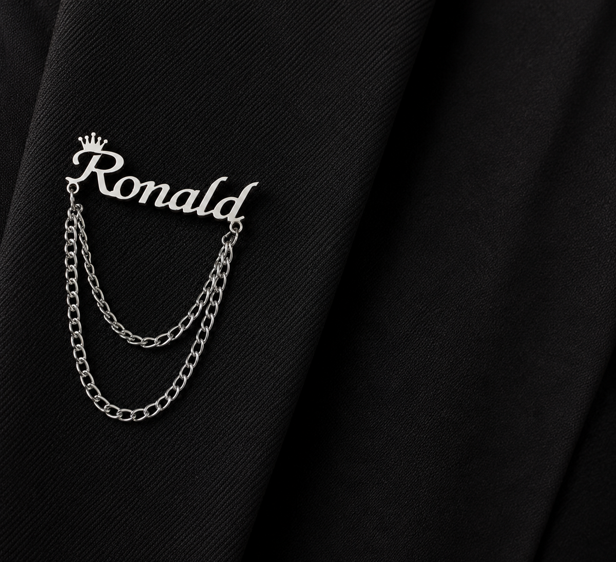 Pin’s AUDACE argenté personnalisé avec le prénom Ronald, couronne et chaînes décoratives sur veste noire