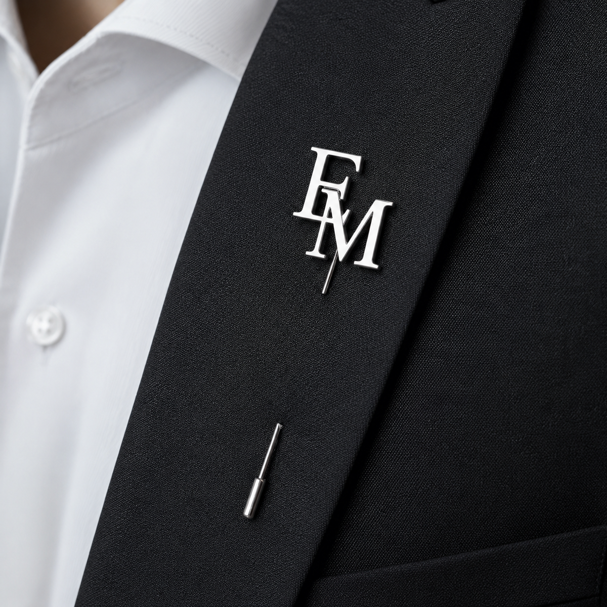 Pin’s à tige ÉLITE argenté personnalisé avec les initiales EM porté sur une veste noire